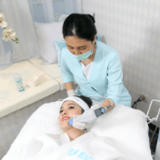 Sandra Dewi in a white robe lying on a treatment bed at Blink Beauty Clinic whilst getting a treatment by a therapist.