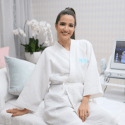 Nia Ramadhani in a white robe at Blink Beauty Clinic sitting on a treatment bed smiling at the camera before her treatment.