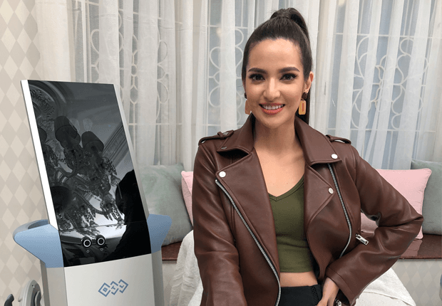 Nia Ramadhani wearing a red jacket and green shirt smiling at the camera next to a BTL emsculpt muscle toning machine at Blink Beauty Clinic.