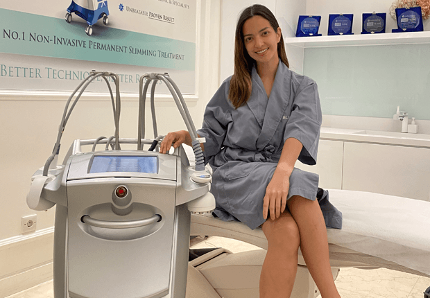 Nia Ramadhani sitting in a grey robe next to a venus legacy machine at Blink Beauty Clinic.